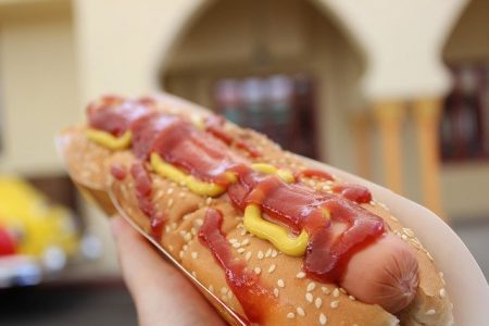A hot dog with ketchup and mustard held in hand
